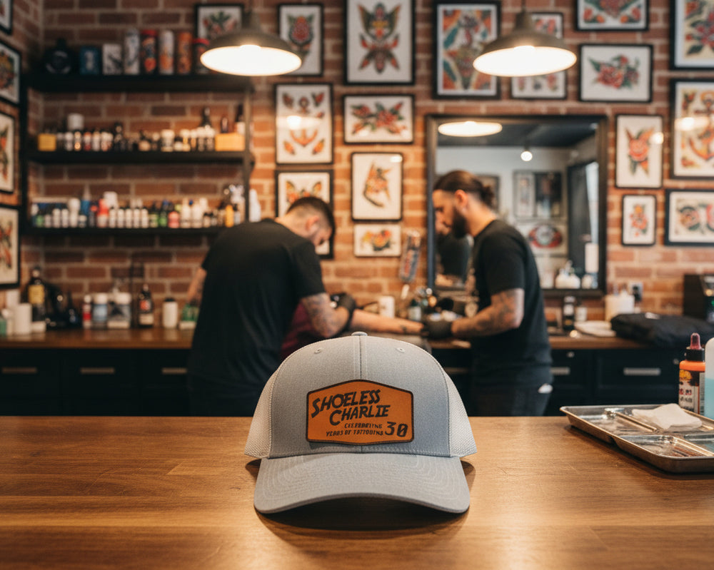 Richardson 112 gray snapback hat with Shoeless Charlie 30th Anniversary leather patch in tattoo shop setting.