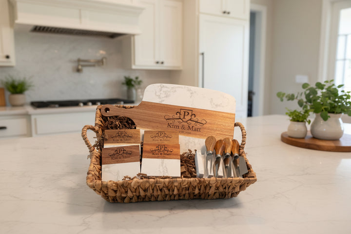 Custom closing gift basket with engraved marble and acacia charcuterie board cheese knives and matching coasters displayed on kitchen counter