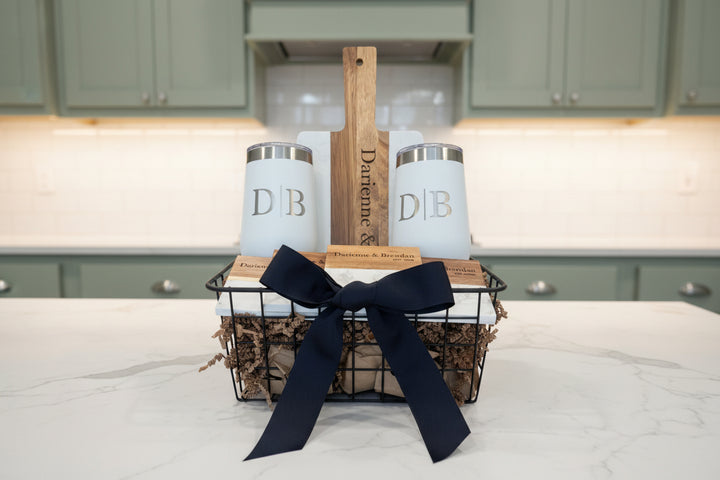 Signature personalized gift basket with engraved marble and acacia charcuterie board, two monogrammed 16oz wine tumblers, and four engraved slate coasters, arranged in a decorative wire basket for housewarming, closing, or realtor gifts
