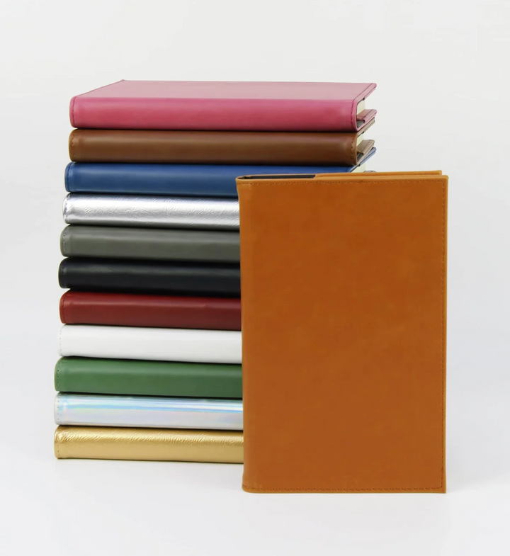 Engraved leatherette journal with multiple color options shown in stack and tan notebook in front personalized custom journal gift