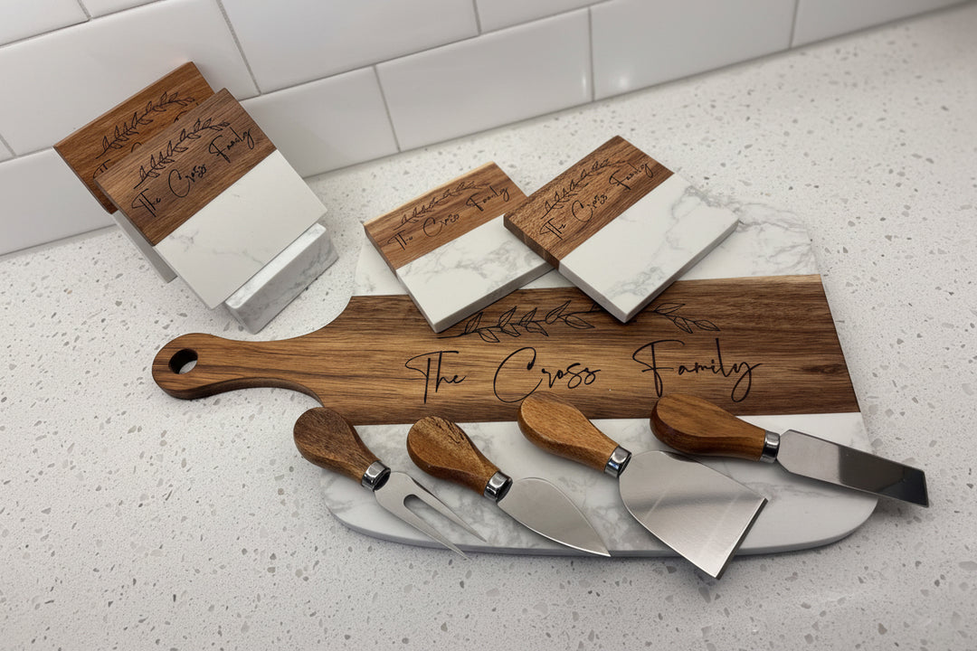 Marble and acacia charcuterie cheese board set with matching cheese knives displayed on kitchen countertop.