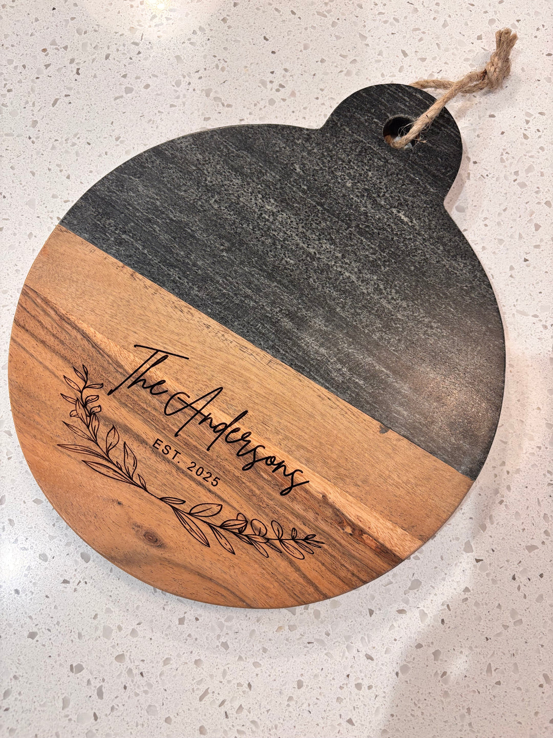 Personalized marble and wood round cutting board engraved with family name, perfect for wedding or housewarming gift.