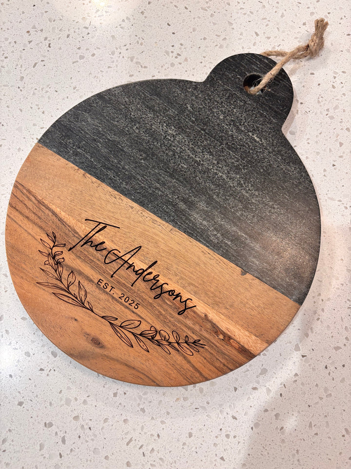 Personalized marble and wood round cutting board engraved with family name, perfect for wedding or housewarming gift.