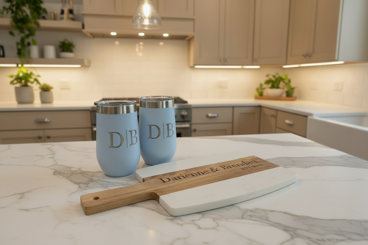 Personalized closing gift set with marble and acacia charcuterie board, engraved coasters, and custom wine tumblers displayed on a kitchen countertop.