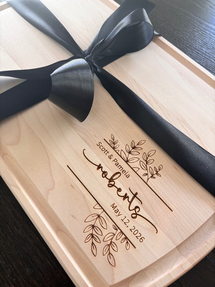 Large arched maple cutting board with custom laser-engraved wedding design, featuring names and wedding date, tied with a black ribbon.