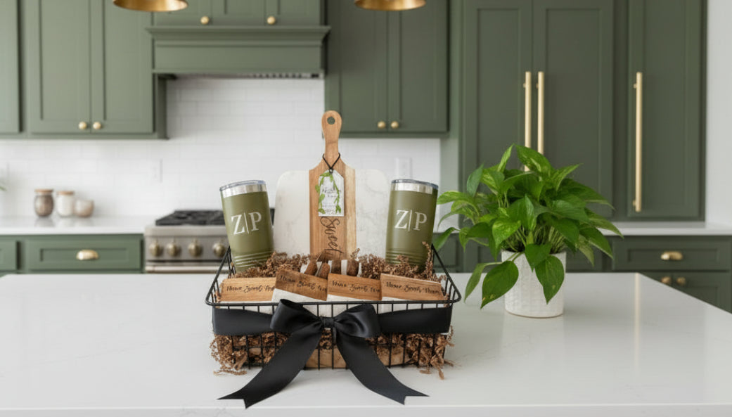 Personalized Signature Plus gift basket with custom tumblers and a marble and acacia wood board, displayed on a white kitchen island with green cabinets.