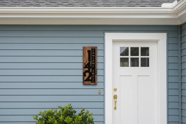 Personalized wooden address sign with house numbers and street name mounted beside a front door on blue siding
