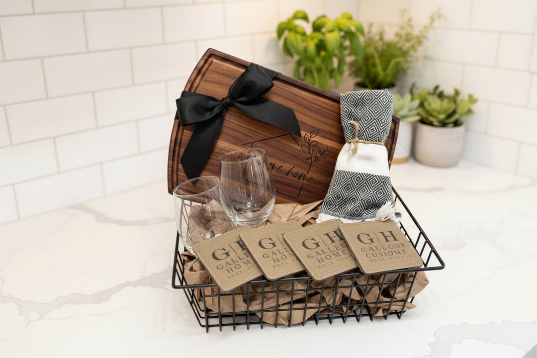 Luxury realtor closing gift basket featuring an engraved wood cutting board, wine glasses, custom logo coasters, and housewarming gift items for new homeowners.