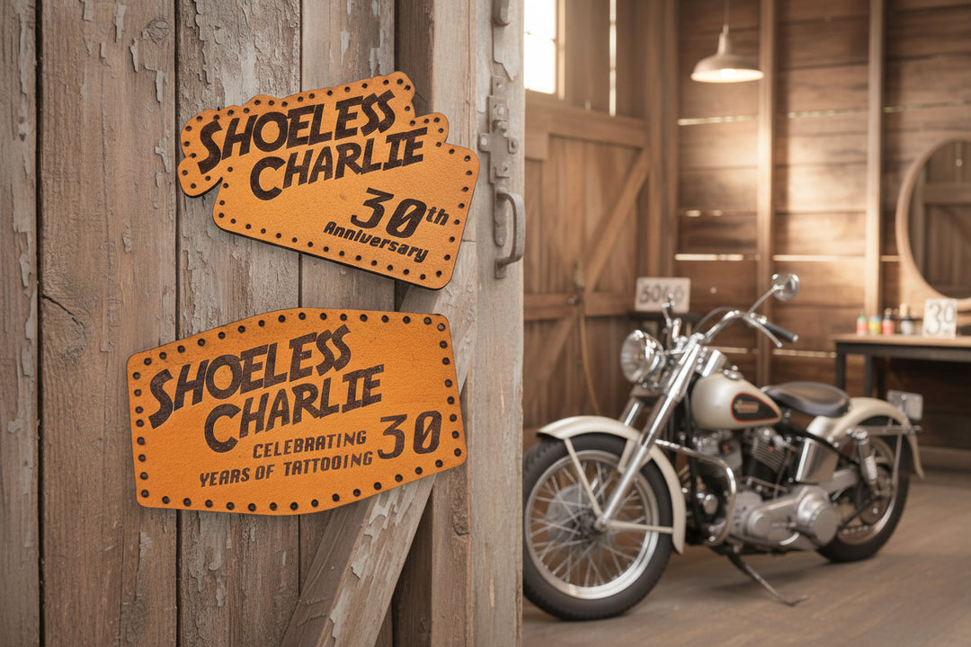 Shoeless Charlie 30th anniversary leather patch displayed on motorcycle in rustic workshop interior with vintage signs and memorabilia.