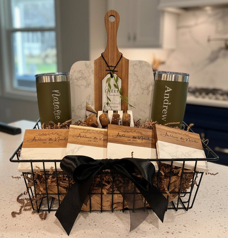 Close up of the Signature Plus gift set featuring olive green tumblers engraved with names, four matching marble and acacia coasters, and a personalized wood tag in a black wire basket.