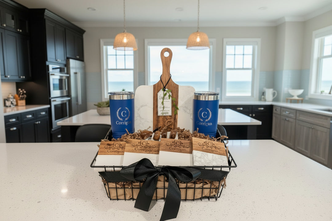 Personalized Signature Plus gift basket on a white counter featuring royal blue custom tumblers, a marble and acacia wood board, and four engraved coasters in a black wire basket with a silk bow.